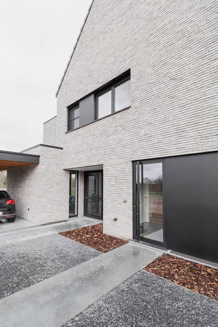 современный клинкерный фасад дома с двухскатной крышей и графитовыми вставками из штукатурки