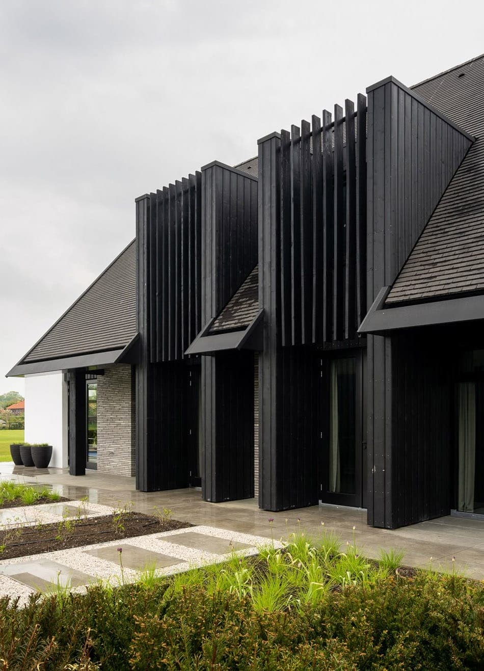 входные группы с графитовыми рейками и доской, кровля - плитка из сланца, декоративная штукатурка и ригельная узкая клинкерная плитка на фасаде дома скандинавского типа