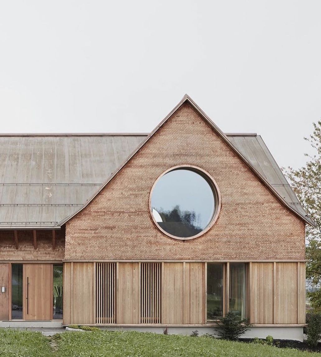 фасад современного коттеджа в бежевых тонах с огромным круглым окном на симметричном фронтоне