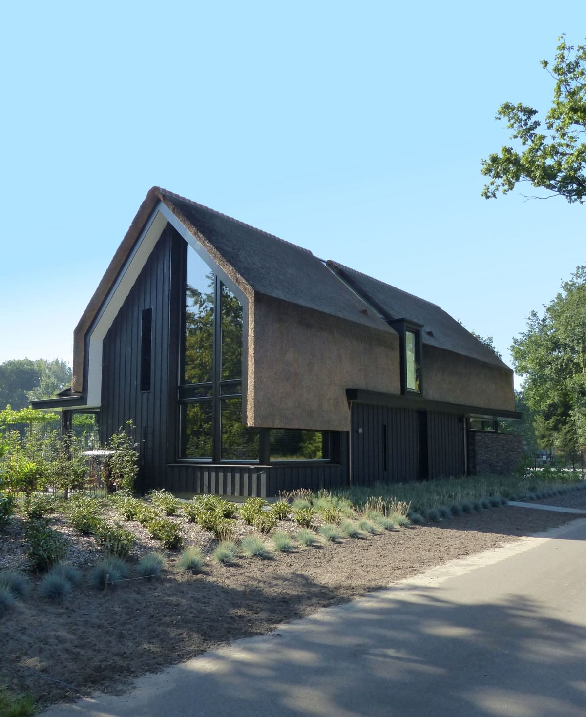 камышовая кровля этого современного барн хауса стильно сочетается с белой акцентной подшивкой свесов и графитовой деревянной отделкой стен