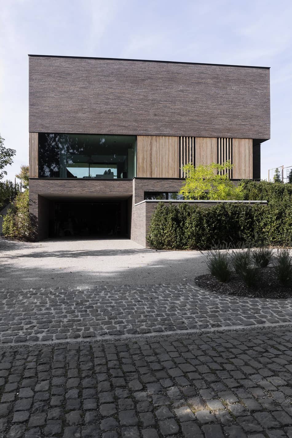 монолитный объем второго этажа в клинкере визуально парит над первым этажом дома благодаря безрамному остеклению большой площади, что характерно для домов в современном стиле