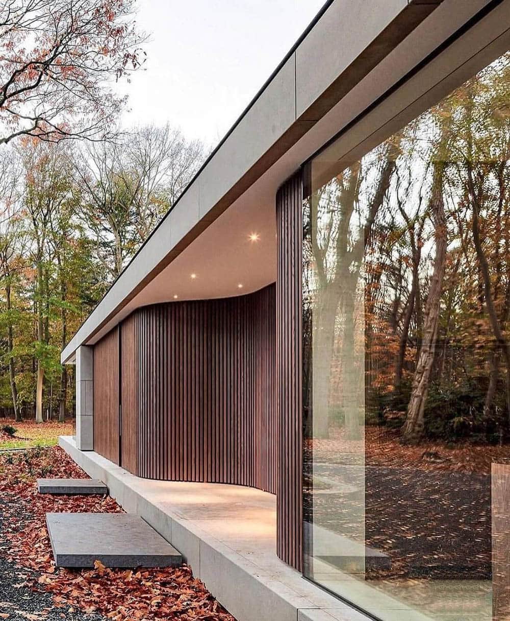 этот уютный одноэтажный дом в современном стиле гармонично сочетает контрастную отделку из вертикальных деревянных реек на стене по типу фасад волна и безрамное остекление