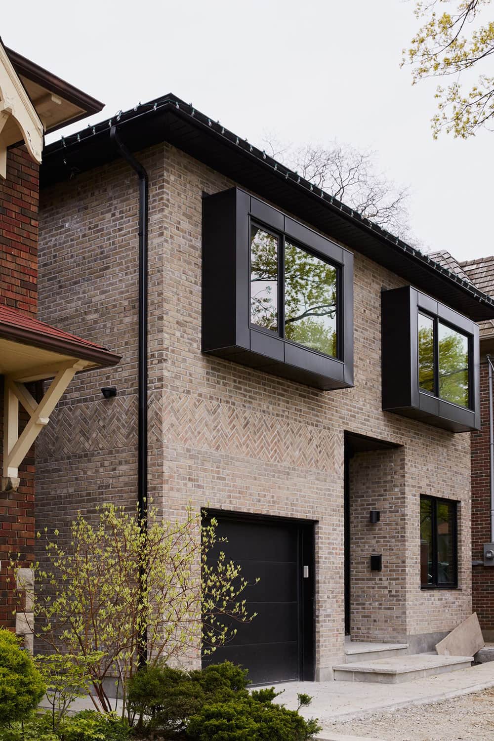 современный фасад небольшого уютного двухэтажного дома с отделкой клинкерной плиткой и выразительными консольными черными окнами