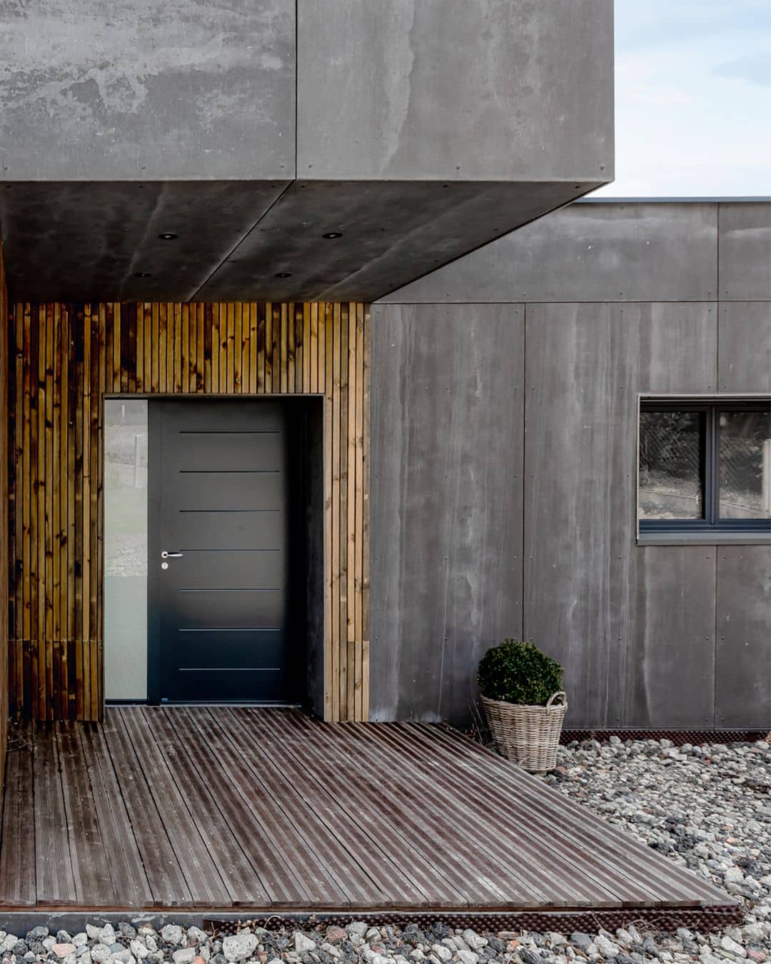 серый фиброцементный фасад этого одноэтажного дома имеет простую и выразительную отделку входной группы узкими досками желтого оттенка с подпалинами