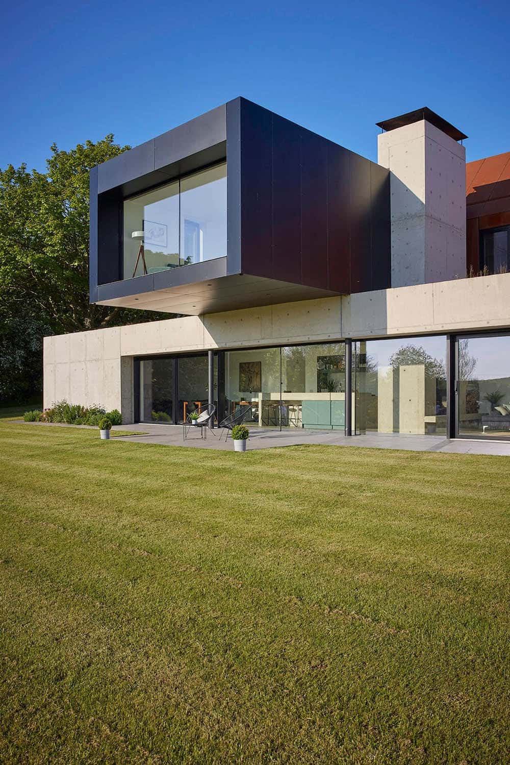 современные по стилю загородные дома нередко решают выразительностью пластики архитектурных объемов - парящий консольный второй этаж в графитовой керамогранитной отделке над первым этажом из бетона и стекла