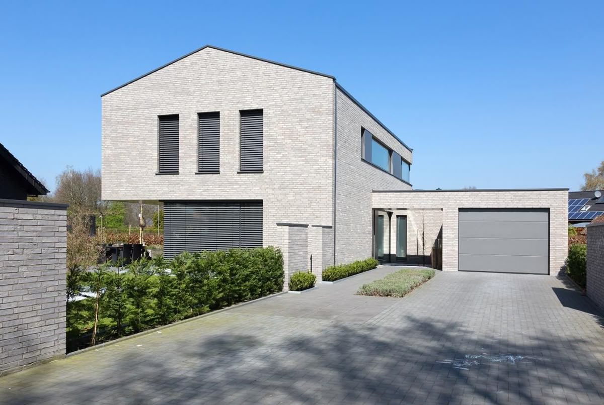 отделка фасадов этого современного минималистичного дома с гаражом выполнена в светло-серой клинкерной плитке, которая хорошо подчеркивает пластику и гармонию архитектурных объемов этого здания