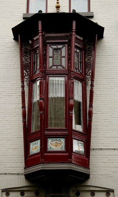 в проекте этого здания фасады притягивают все внимание к деревянному эркеру вишневого цвета на кирпичной белой стене - фото фрагмента