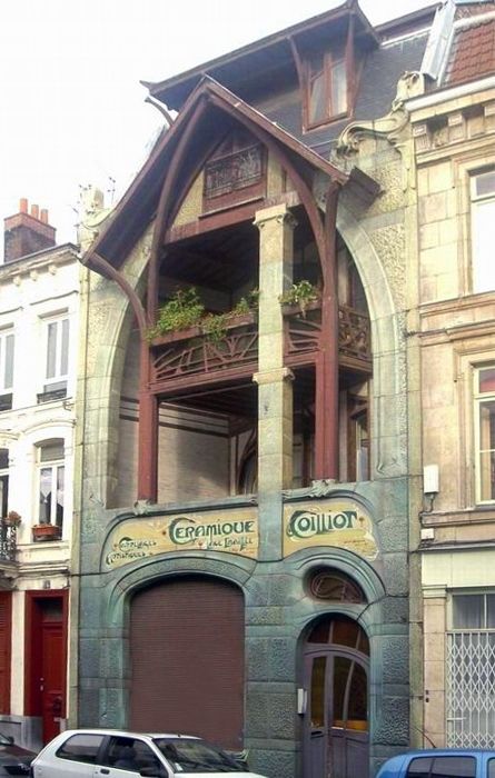 бежевый каменный фасад здания в стиле модерн с интересным решением балкона над входной группой и деревянными элементами