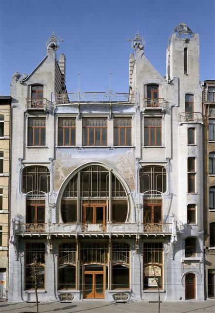 трехэтажное симметричное здание эпохи модерна с угловой башней и оштукатуренными фасадами белого цвета с фреской